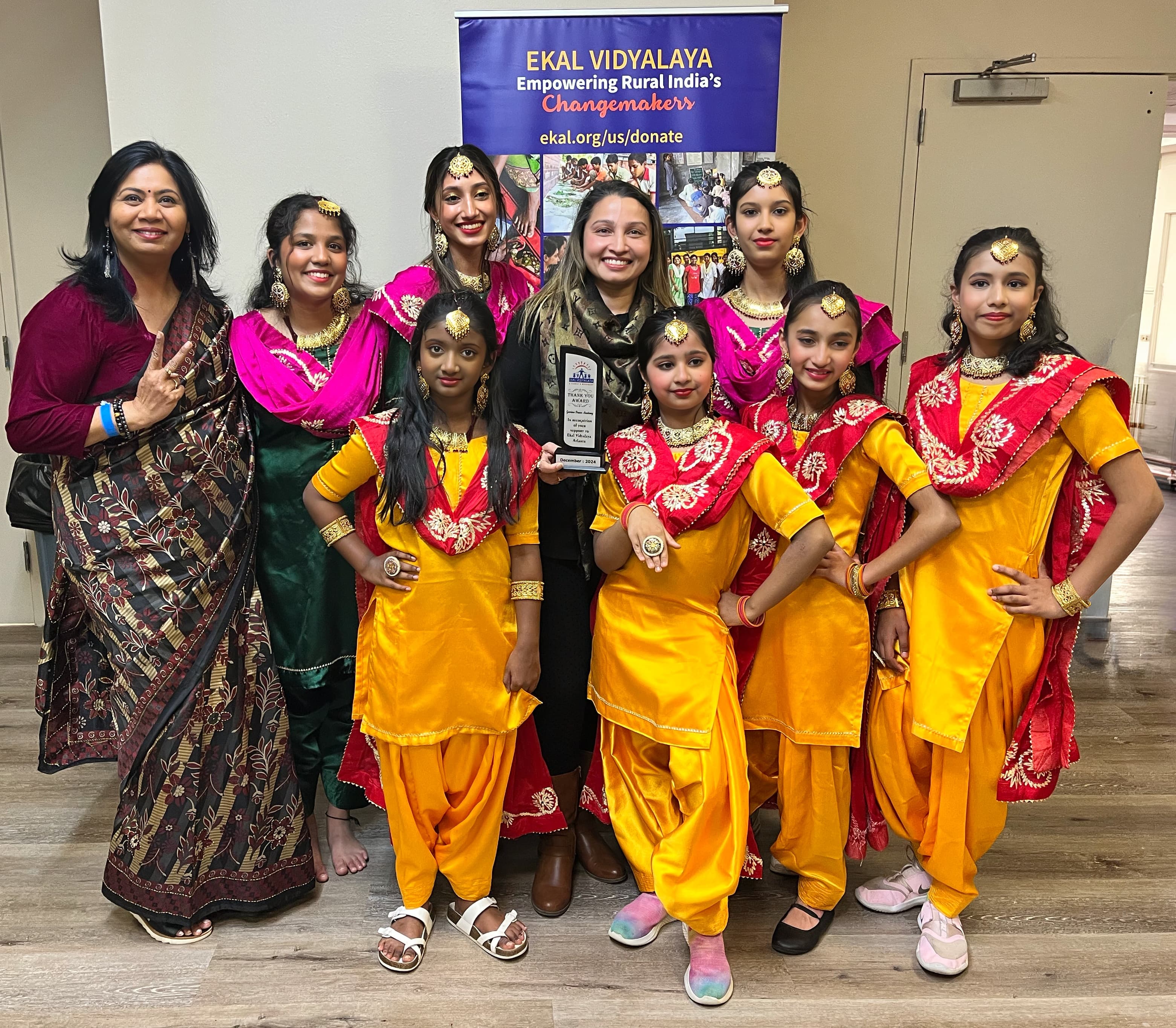 Garima Dance Academy students with the instructor at an Ekal Vidyalaya charity event, holding a recognition plaque